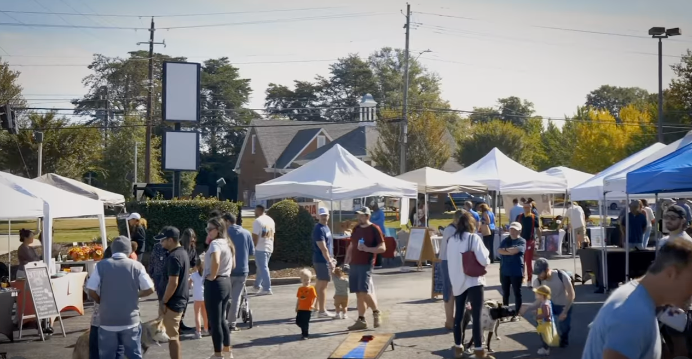 White vendor tents and families walking through the Dunwoody plaza market